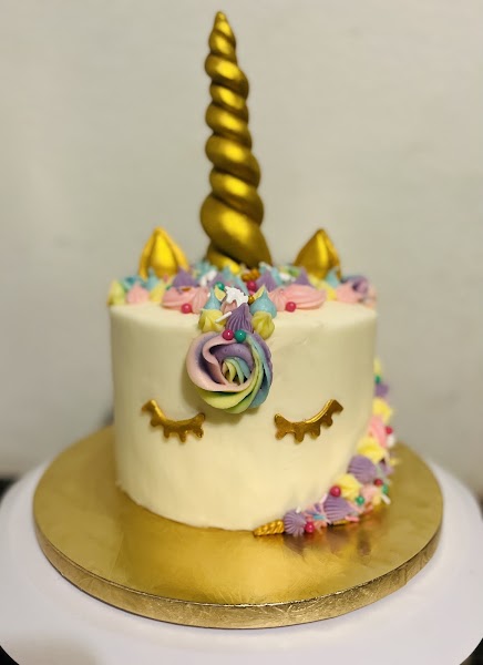 Whimsical unicorn cake with gold horn, pastel rainbow flowers, and fondant details