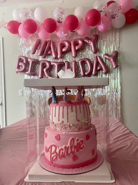 Two-tier pink Barbie themed birthday cake with drip frosting and Barbie doll toppers